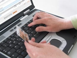Image of hand holding credit card, other typing on computer keyboard