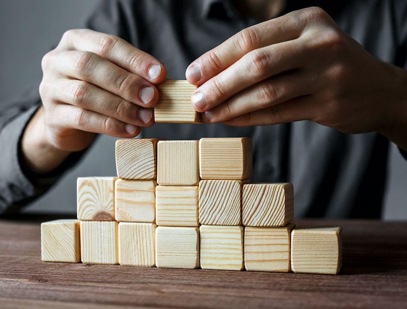 Man's hands creating wooden building block pyramid - structure your online course concept