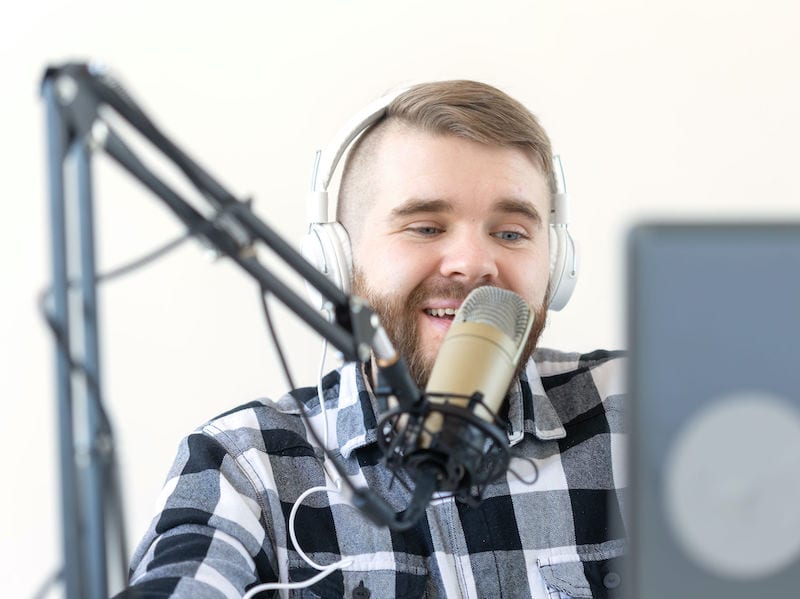 Bearded young man with mic on boom at laptop - podcast content marketing concept